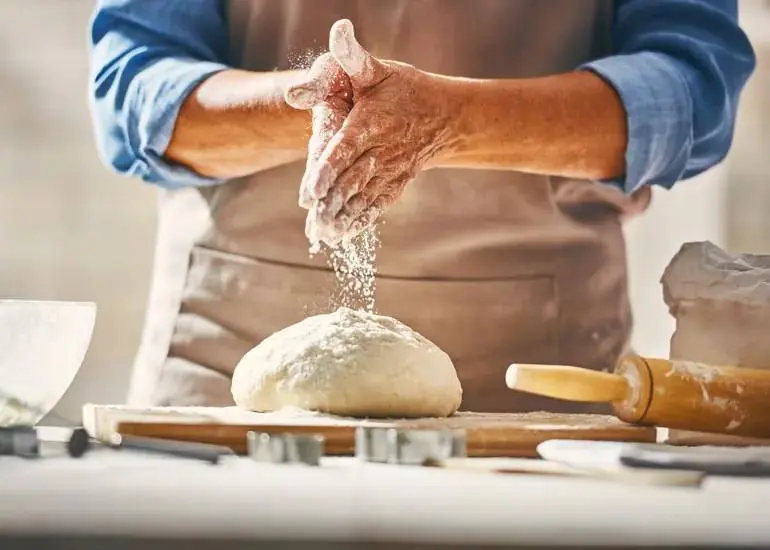 A baker sprinkles flour on a ball of bread dough.