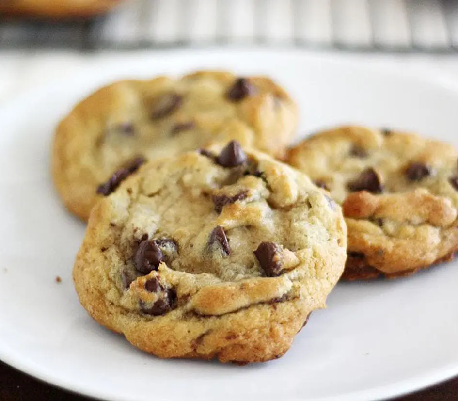 Plate of three warm chocolate chip cookies by a cooling rack