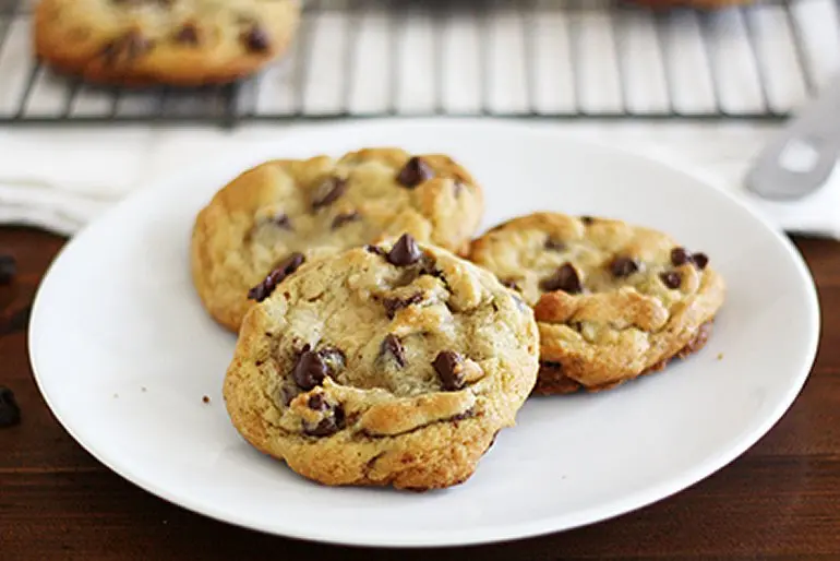 Plate of three warm chocolate chip cookies by a cooling rack