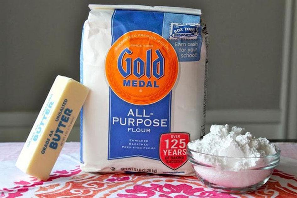 A bag of gold medal all purpose flour, a stick of butter and a bowl of flour placed on a table.