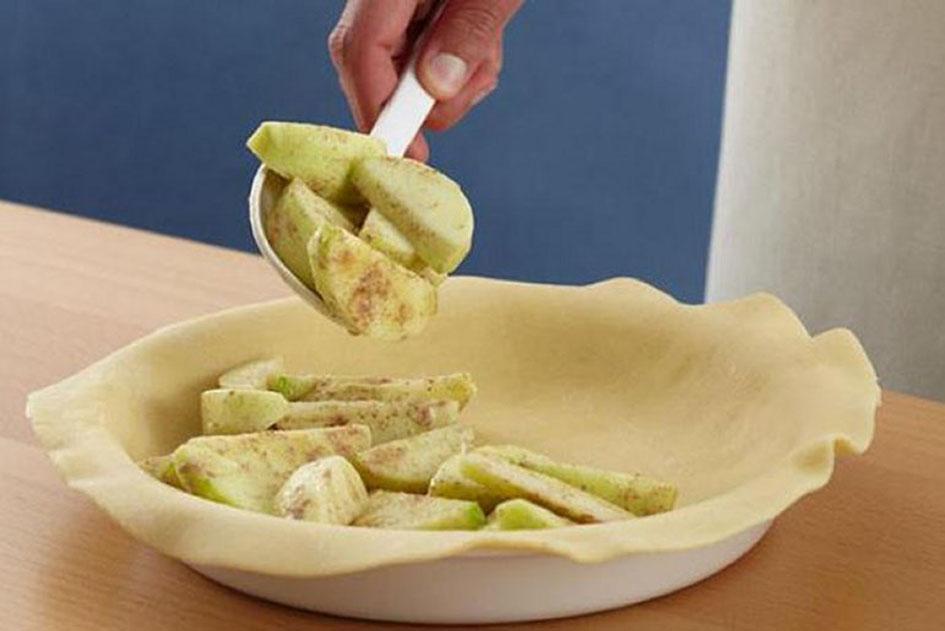 Picture of a hand adding filling over a pastry with a spoon.