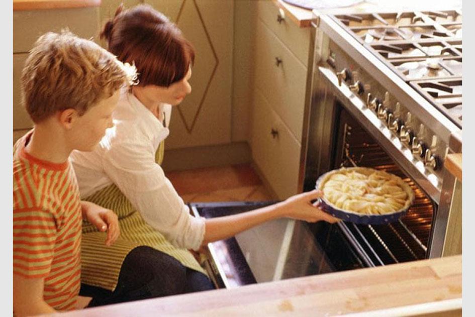 Baking with Kids - A woman and a boy carefully placing a pie into the oven, preparing it for baking