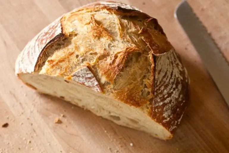 Cut half loaf of fresh bread with bread knife on cutting board