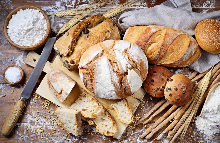 Top down view of several loaves of artisan bread haphazardly set on a kitchen workspace.